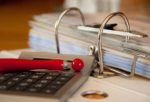 An open folder next to a calculator and red pen
