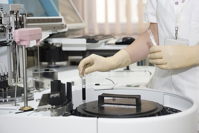 A centrifuge with a lab worker wearing gloves holding a test tube