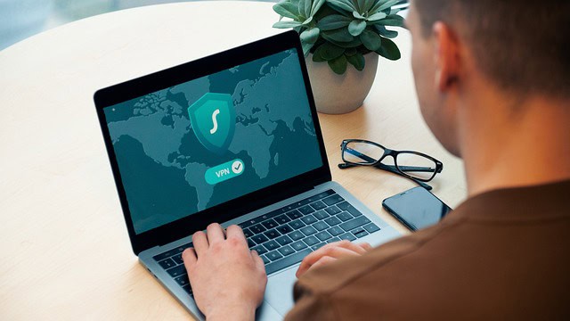 A person logging into a secure website, with his glasses and phone resting next to the laptop